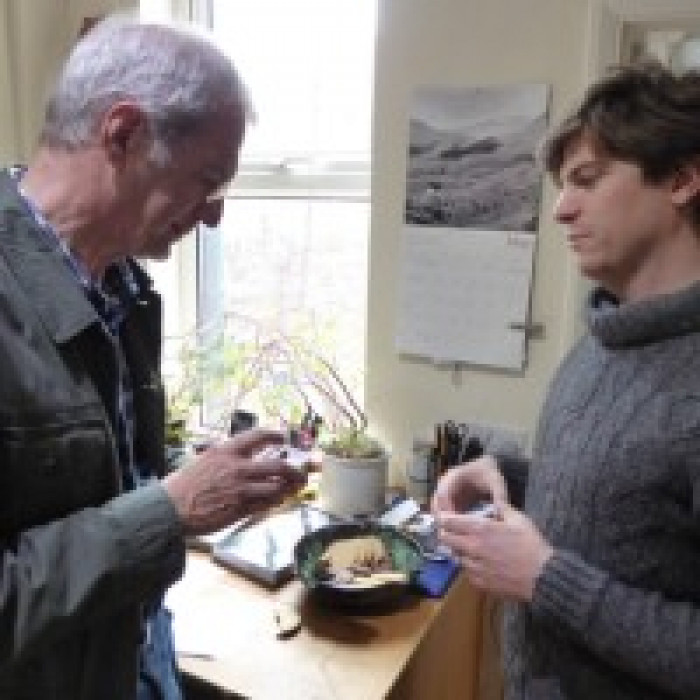 Tomas and a visitor looking at energy saving equpment both are male and wearing jumpers and coats, both are white, one has short white hair and glasses, the other has slightly longer brown hair that sweeps over his forehead.