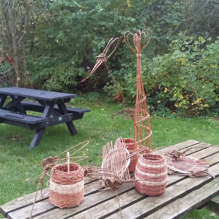 A selection of items made by the willow weaving group including baskets, bird feeders and ornamnts are sitting on a table in the garden.