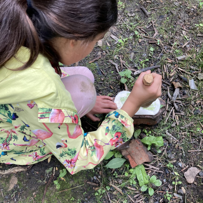 A child is making leaf art using cotton and a wooden tool.