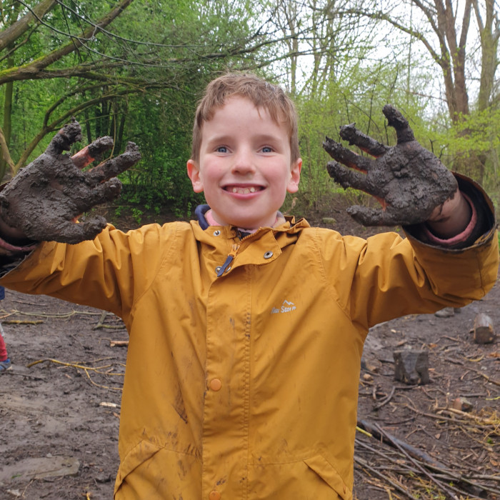 A smiling boy in the woodland area with very muddy hands