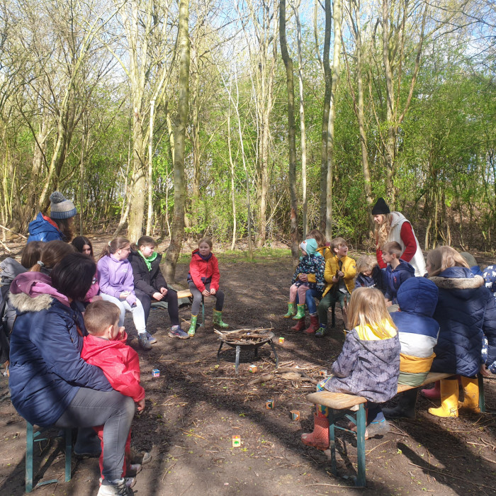 A group of children sit around the fire circle.