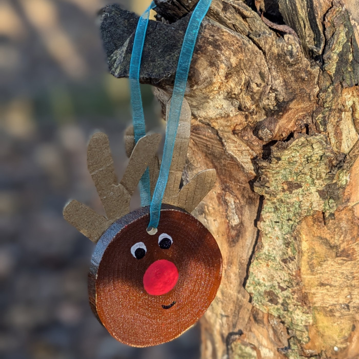 handmade reindeer decoration made from wood and cardboard is hanging from a blue ribbon on tree branch