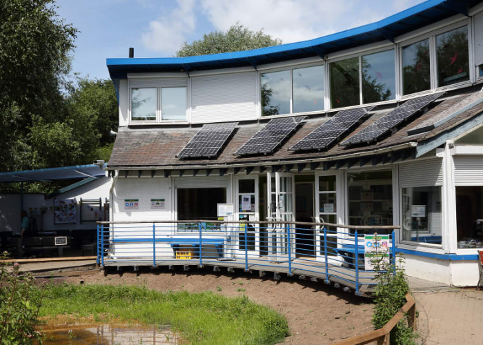 A photo of the St Nicks environment centre, it's a curved white building with blue trimings, solar panels a large pond and benches