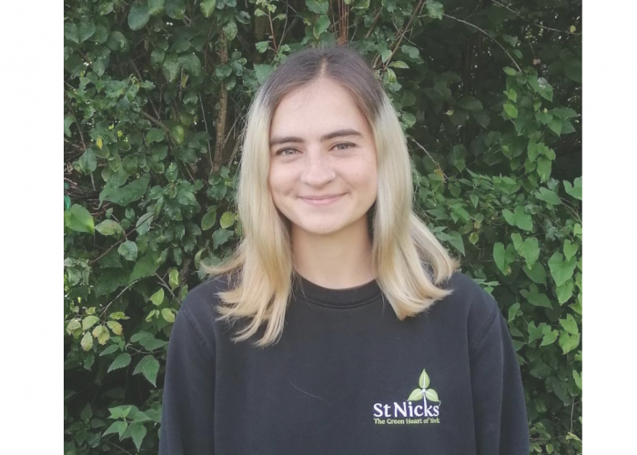 Maeve is a young woman with a nose ring smiling into the camera, she has shoulder length hair with dark roots and blonde ends