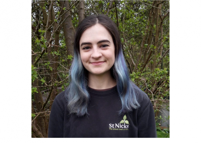 Maeve is a young woman smiling into the camera, she has shoulder length hair with dark roots and blue ends