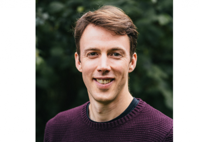 Stuart is a white male with brown hair that is longer on top than it is at the sides, he is looking straight into the camera and smiling.