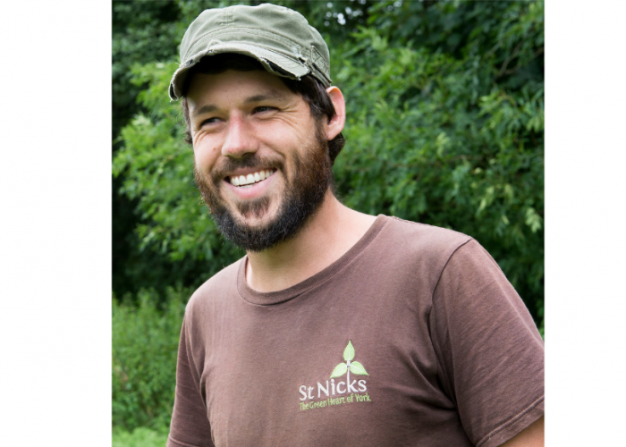 Jonathan is a young man wearing a green cap, he has dark hair poking out of the front of his hat and a dark beard he is looking to the left of the camera and laughing