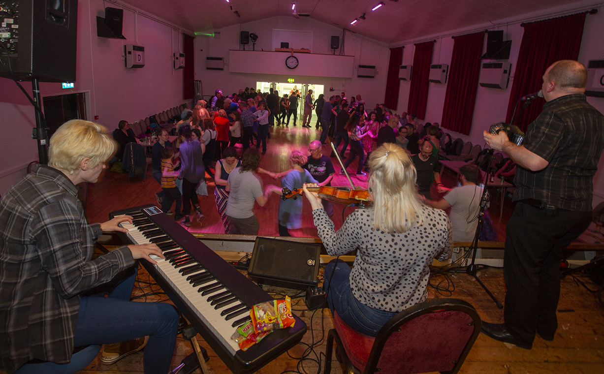 Ceilidh band in foreground with dancers in circles in the background