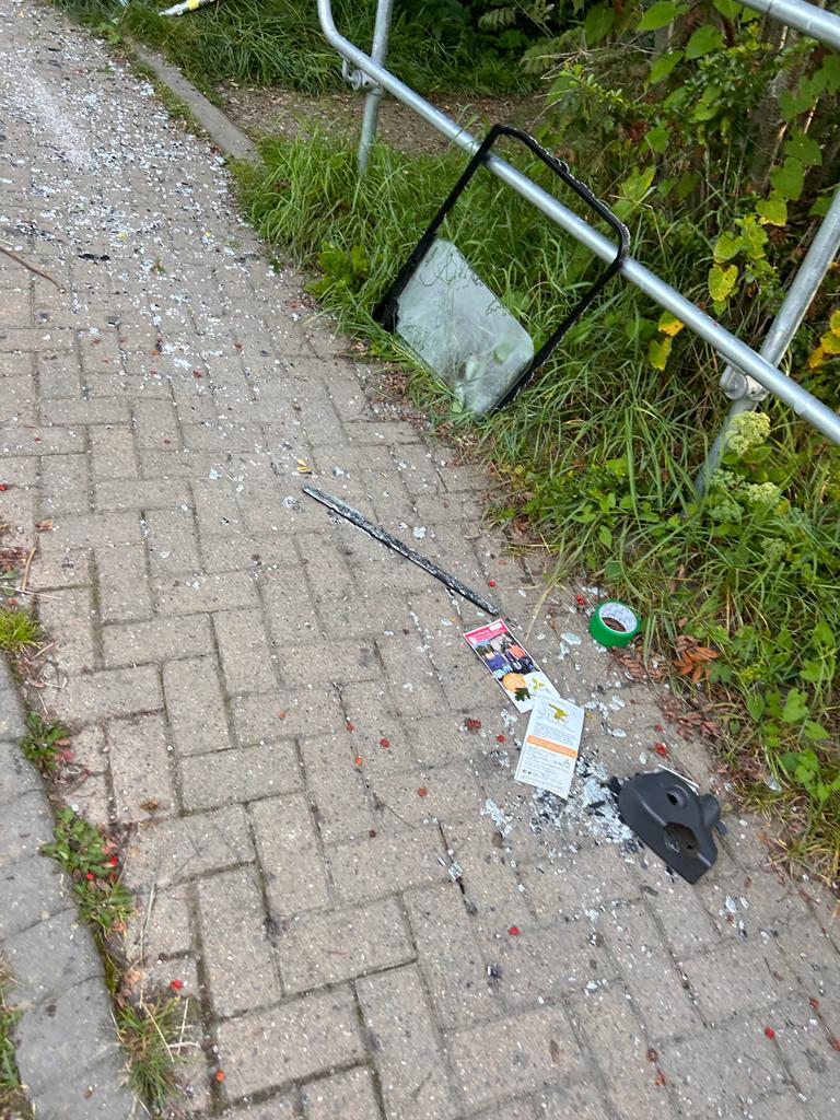 A trail of glass, vehicle parts including a car window frame and other debris litters the path all the way up to the environment centre garden