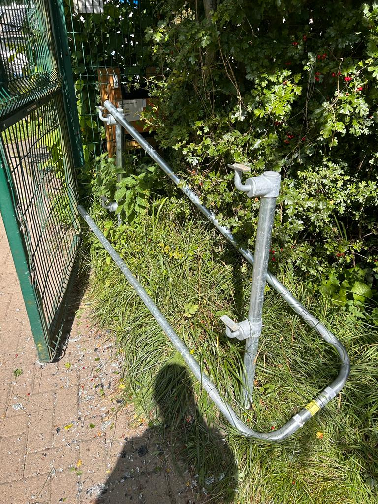 A close up photo of the handrail that leads into the garden of st nicks it has been snapped off and hangs off a wonky post. to the left of the image is a wonky gate where the base is bent out of shape. There is lots of glass on the floor.