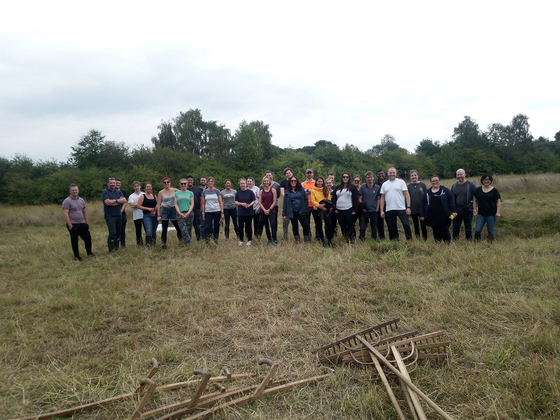 A large group of people standing in front of rakes and scythes.